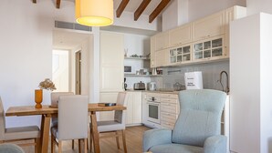 A modern kitchen with white cabinets, a dining area with a wooden table and chairs, and a light blue armchair. - Townhouse with puig de Maria view by home villas 360 (Pollensa)