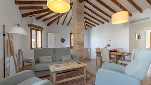 A spacious living area with a wooden ceiling, a sofa, a coffee table, and a dining table with chairs. - Townhouse with puig de Maria view by home villas 360 (Pollensa)