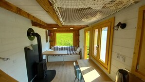 Ein gemütliches Blockhaus-Interieur mit Holzbalkendecke, fest eingebautem Herd, einer Sitzecke mit Sofa und Tisch und großen Fenstern, die viel Tageslicht hereinlassen.