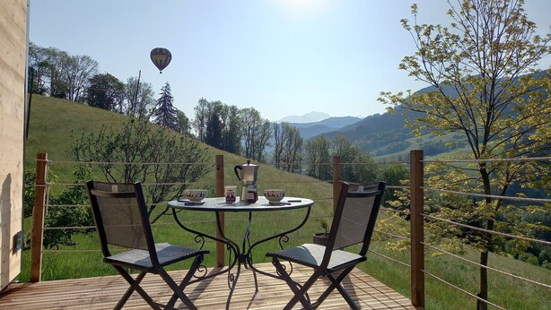 Eine Terrasse mit Tisch und zwei Stühlen, mit Blick auf eine reizvolle Landschaft mit Hügeln und einem ferngesetzten Heißluftballon.