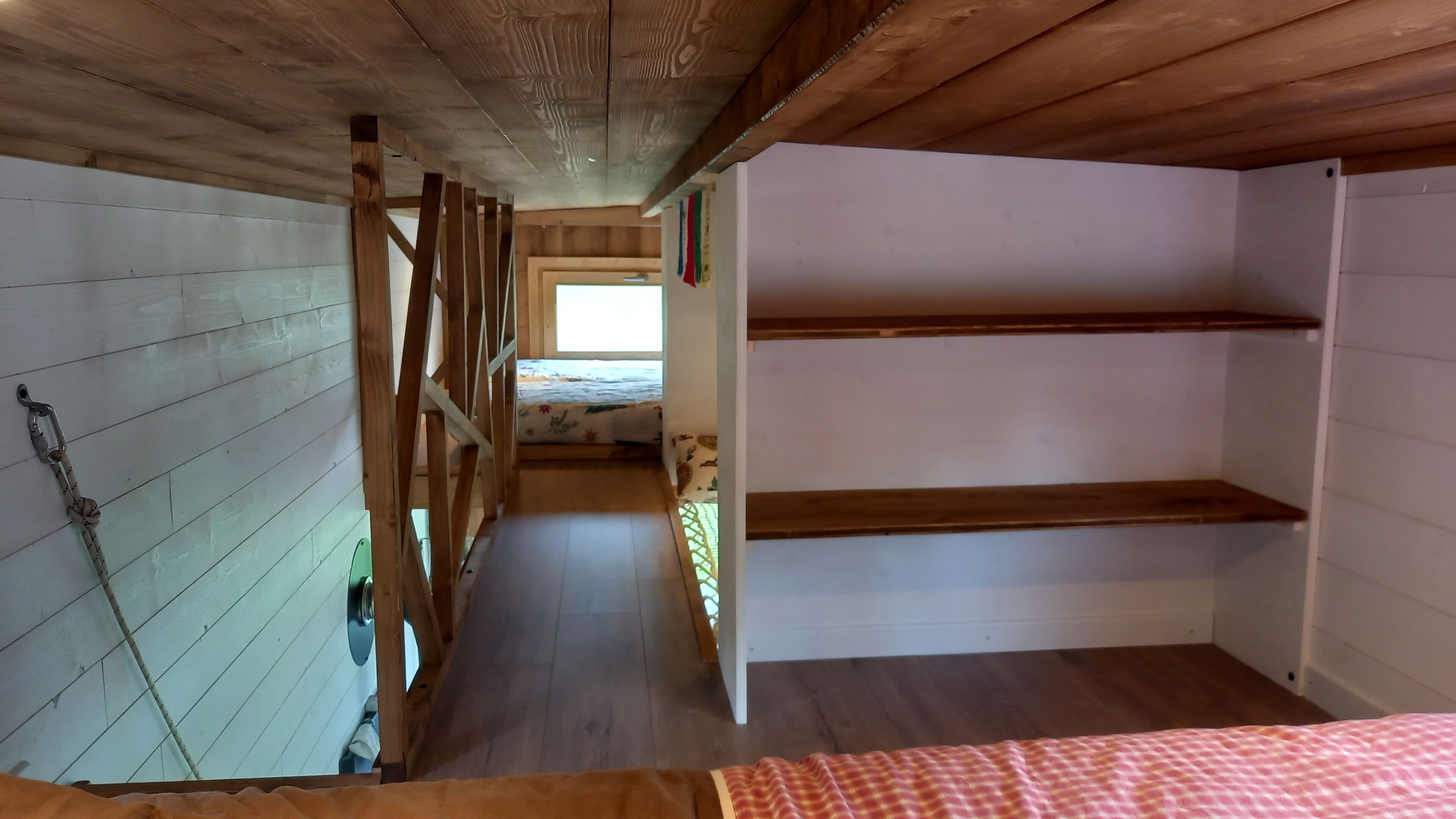 Um corredor estreito com vigas de madeira no teto e uma cama com cobertor xadrez no final.