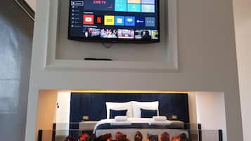 Habitació d'hotel moderna amb televisió de pantalla plana penjada sobre un llit, una taula de cafè de vidre amb objectes decoratius i un panell de capçal de llit de color fosc.