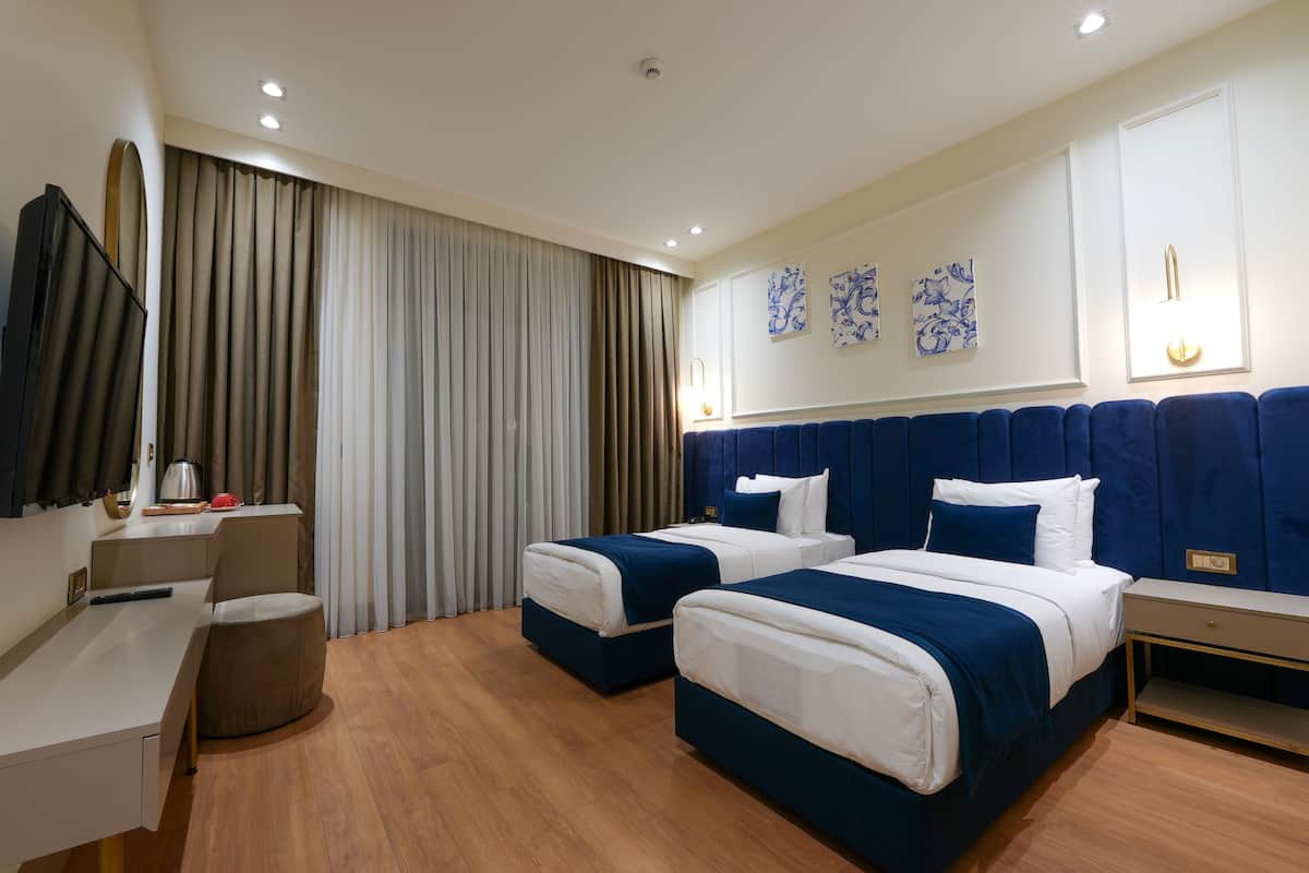 A hotel room with two beds, a desk, a chair, and a large window with curtains.