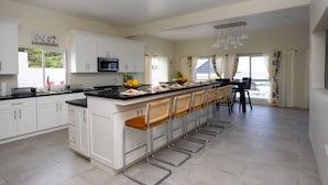 Una cocina moderna con armarios blancos, una isla central con taburetes de bar, un microondas y un comedor con mesa y sillas.