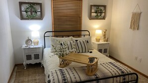 Ein ordentlich eingerichtetes Schlafzimmer mit einem Bett, Nachttischen, einem Beistelltisch, einem Holztablett und einem gewebten Teppich.