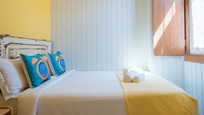 A bed with white bedding, two blue pillows with a circular design, and a yellow blanket. - Casa Pé N'Areia (Ferrel)