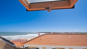 A view from a window overlooking a beach with a tiled roof and a wooden structure in the foreground. - Casa Pé N'Areia (Ferrel)