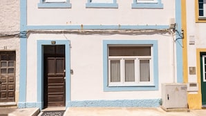 A two-story building with a blue and white facade, a tiled roof, and a cobblestone street. - Casa Pé N'Areia (Ferrel)
