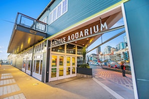 Het gebouw van het Seattle Aquarium, met een glazen ingang en een uitzicht op de skyline op de achtergrond.
