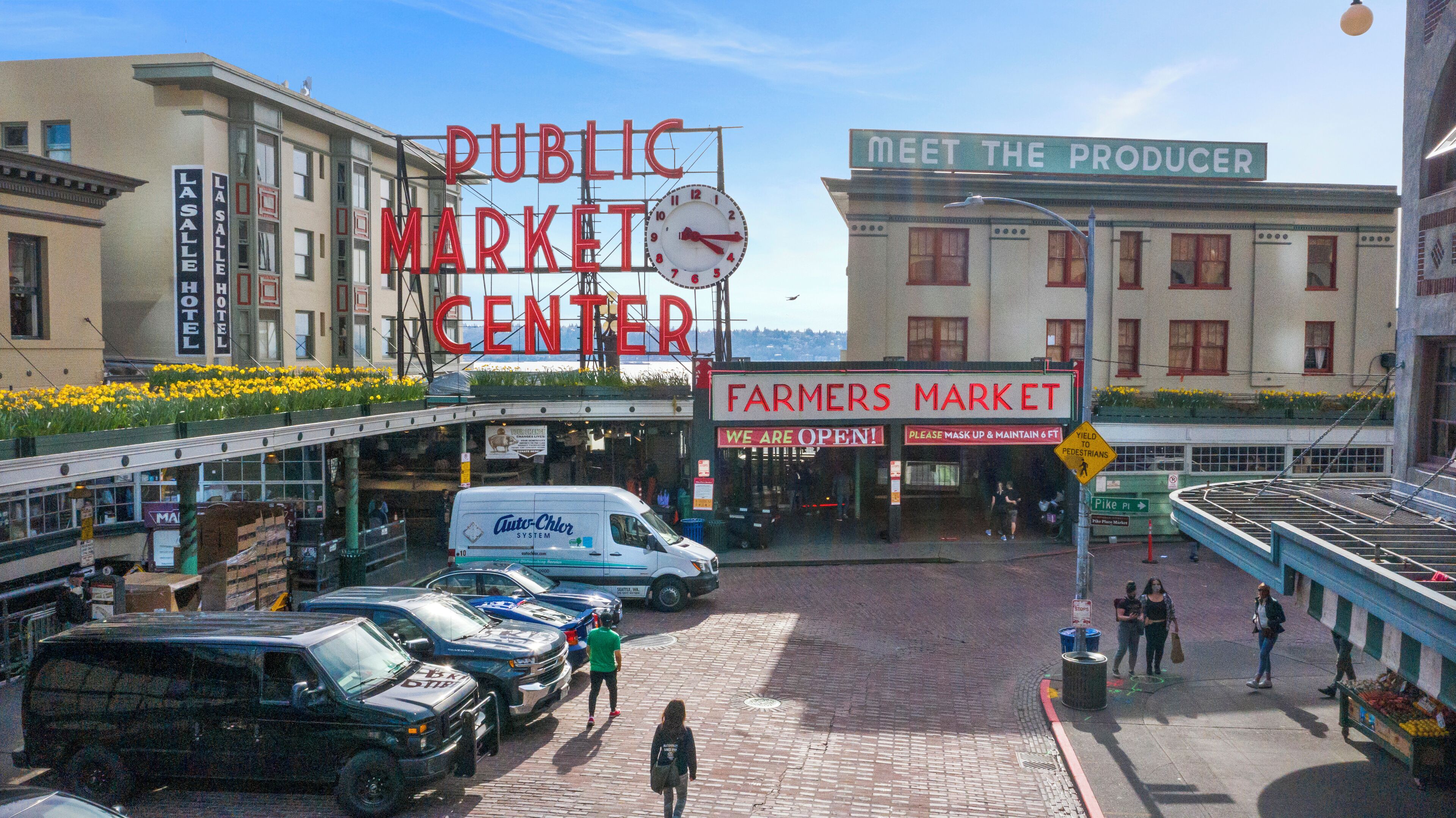 Un marché public doté d’une horloge, d’une enseigne indiquant « Marché de producteurs » et d’une autre enseigne indiquant « Rencontrez les producteurs ».