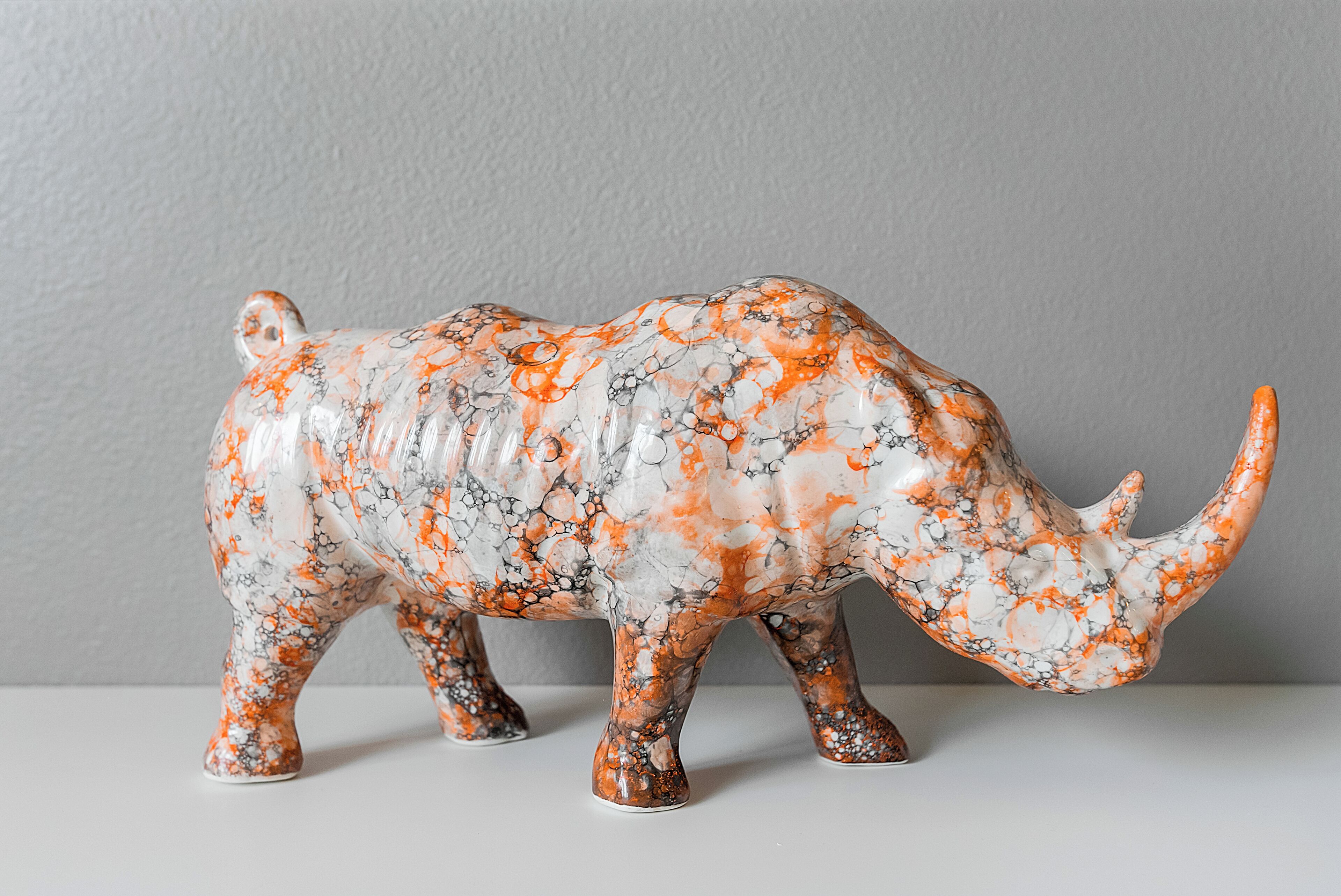 Une figurine de rhinocéros en céramique, avec un motif marbré blanc et orange.