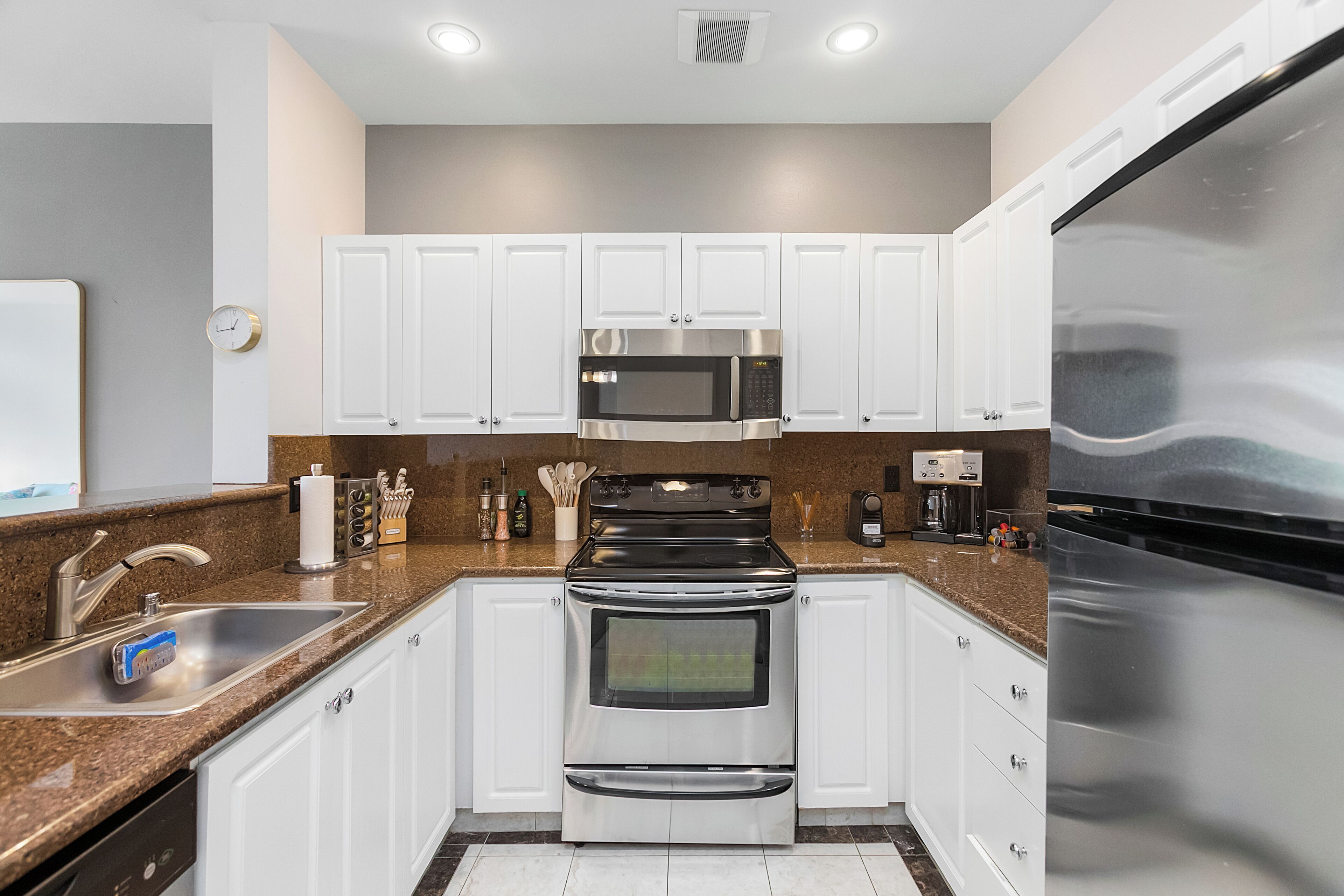 Una cocina moderna con armarios blancos, electrodomésticos de acero inoxidable, un lavamanos doble y un refrigerador.