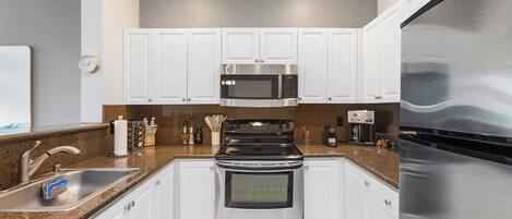 Una cocina moderna con armarios blancos, electrodomésticos de acero inoxidable, un lavamanos doble y un refrigerador.