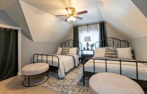 Two single beds with metal frames and white bedding, accompanied by matching ottomans and a ceiling fan with a light fixture.