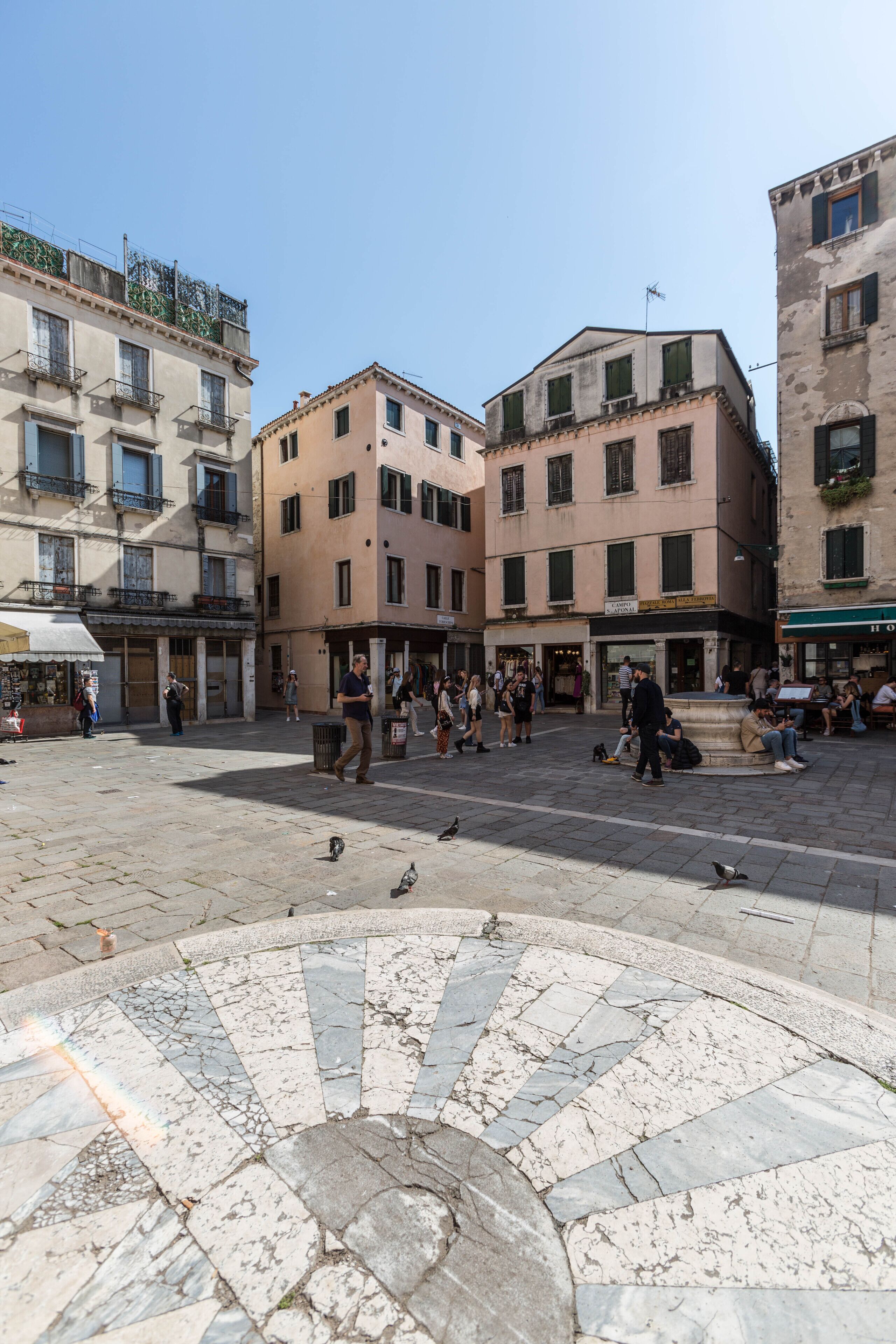 A public square with historic buildings, a fountain, and people walking.