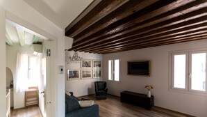 A living room with a wooden ceiling, a sofa, a chair, a TV, and framed pictures on the wall. - Aponalview apartment  027042-LOC-12481 (Venezia)