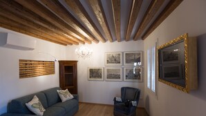A room with a wooden ceiling, a blue sofa, a chair, a wooden bench, and a wall with framed pictures. - Aponalview apartment  027042-LOC-12481 (Venezia)