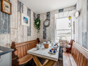 Un comedor rústico con paredes de madera, un banco, una mesa dispuesta con platos y vistas al mar a través de una ventana.