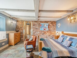 Une pièce avec un mur en briques, un lit avec une literie à rayures, une commode en bois, une chaise et un tableau représentant un paysage portuaire.