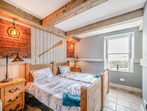 Un dormitorio con techo de madera, pared de ladrillo, una ventana y una cama con ropa de cama estampada.