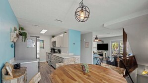 A modern kitchen with white cabinets, a wooden dining table, and hanging plants. - Bikini Bottom *Destin Harbor* Private Gated Beach! (Destin)