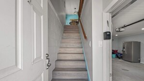 A staircase with a wooden finish, a blue accent wall, and a modern kitchen area with a stainless steel refrigerator. - Bikini Bottom *Destin Harbor* Private Gated Beach! (Destin)