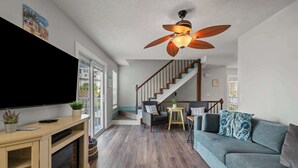 A living room with a flat-screen TV, wooden entertainment unit, grey sofa, and a ceiling fan. - Bikini Bottom *Destin Harbor* Private Gated Beach! (Destin)