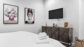 Une chambre à coucher moderne, avec un lit, une commode en bois foncé, un téléviseur à écran plat et deux tableaux encadrés accrochés au mur.