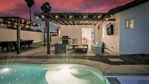 Un jardin avec une piscine, un espace salon extérieur, un coin barbecue et des guirlandes lumineuses.