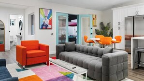 Un salon moderne avec un canapé d’angle gris, un fauteuil orange et un tapis coloré.