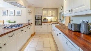 Une cuisine moderne avec des meubles blancs, un plan de travail en bois et des appareils électroménagers intégrés, notamment une cuisinière, un four et un four à micro-ondes.