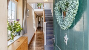 Un couloir avec un banc en bois, une plante en pot, un escalier et une porte verte ornée d’une guirlande.