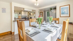 Un coin repas avec une table dressée pour quatre personnes, des chaises en bois et une vue sur la cuisine.