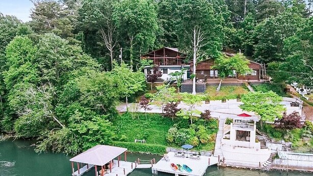En ejendom ved søen med en anløbsbro, et overdækket pavillon og et hus omgivet af frodig vegetation.