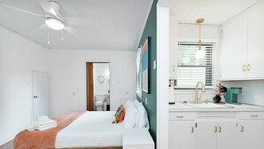 Et soveværelse med en seng, et natbord, en ventilator i loftet og udsigt til det tilstødende badeværelse.