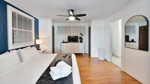 A modern hotel room with a bed, a ceiling fan, a TV, a dresser, and a mirror. - Lake Hickory Trio 3BR Blue Unit (Catawba County)