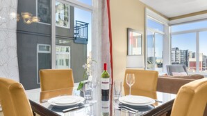 A dining area with a glass table, yellow chairs, a wine bottle, and a city view through large windows. - Corner Unit in the Middle of It All (Seattle)