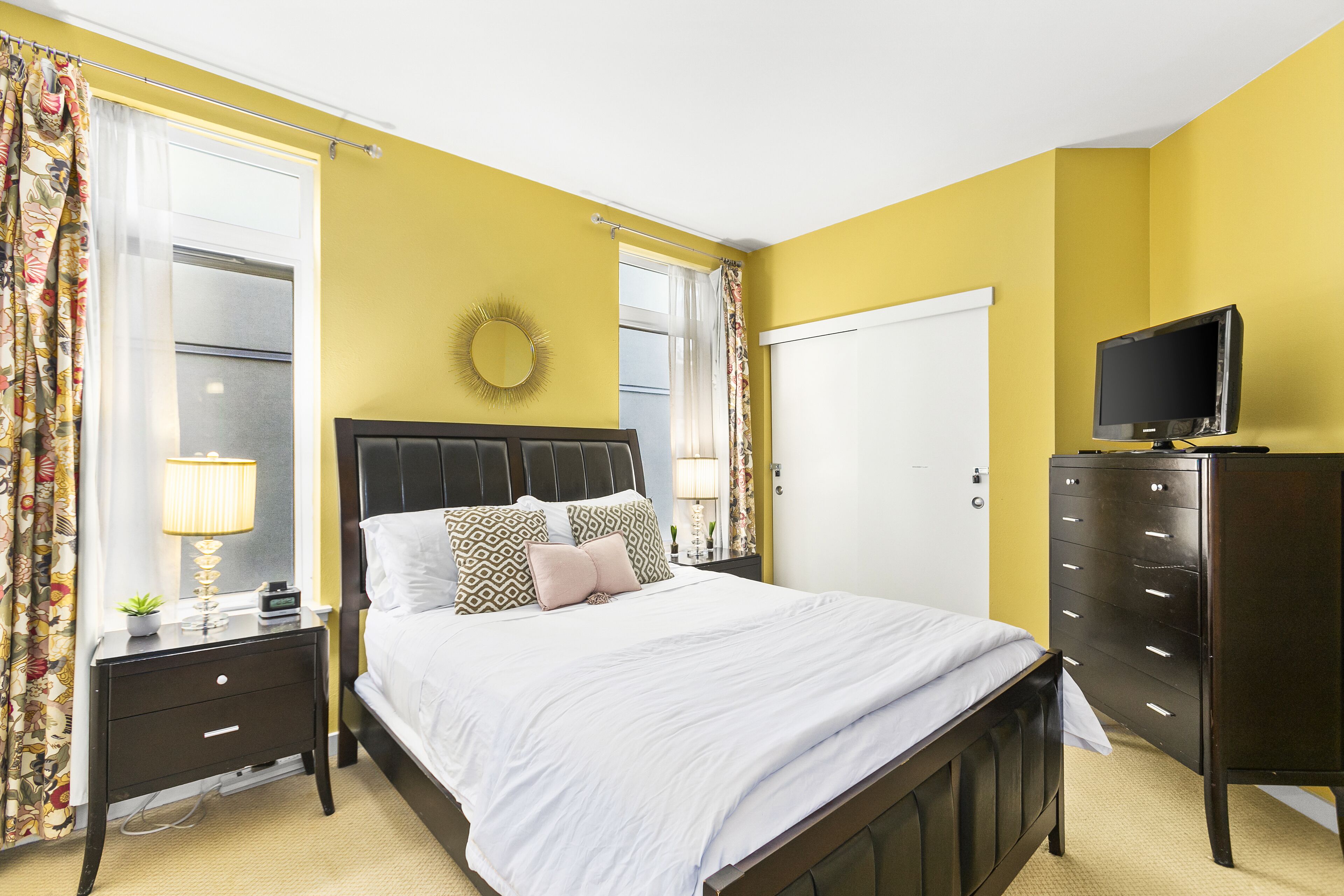 A bedroom with a bed, nightstands, a dresser, a television, and a window with curtains.