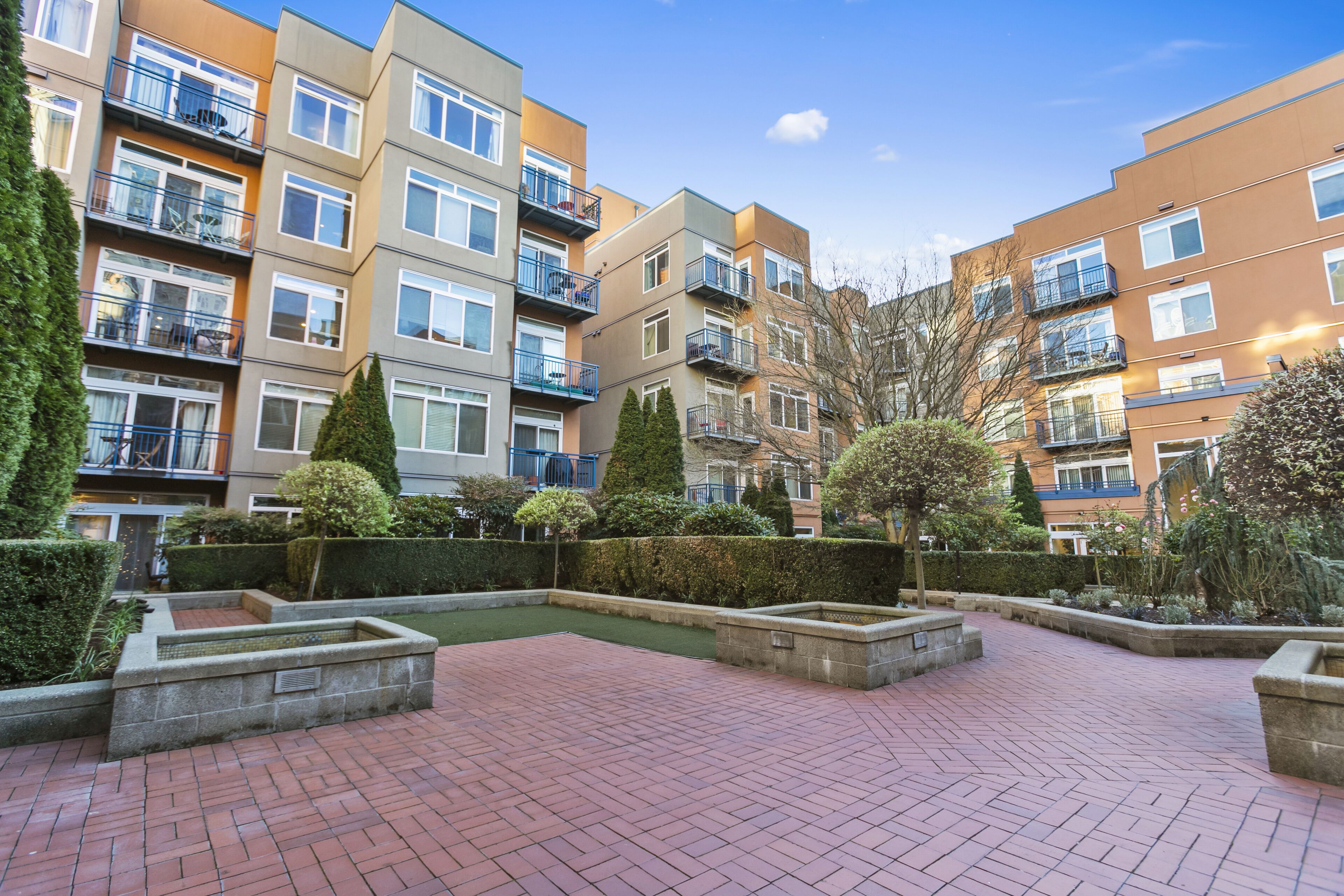 A multi-story residential building with balconies, a paved courtyard, and well-maintained landscaping.