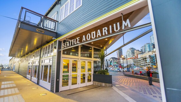The Seattle Aquarium building with a glass entrance and a view of the cityscape in the background. - Corner Unit in the Middle of It All (Seattle)