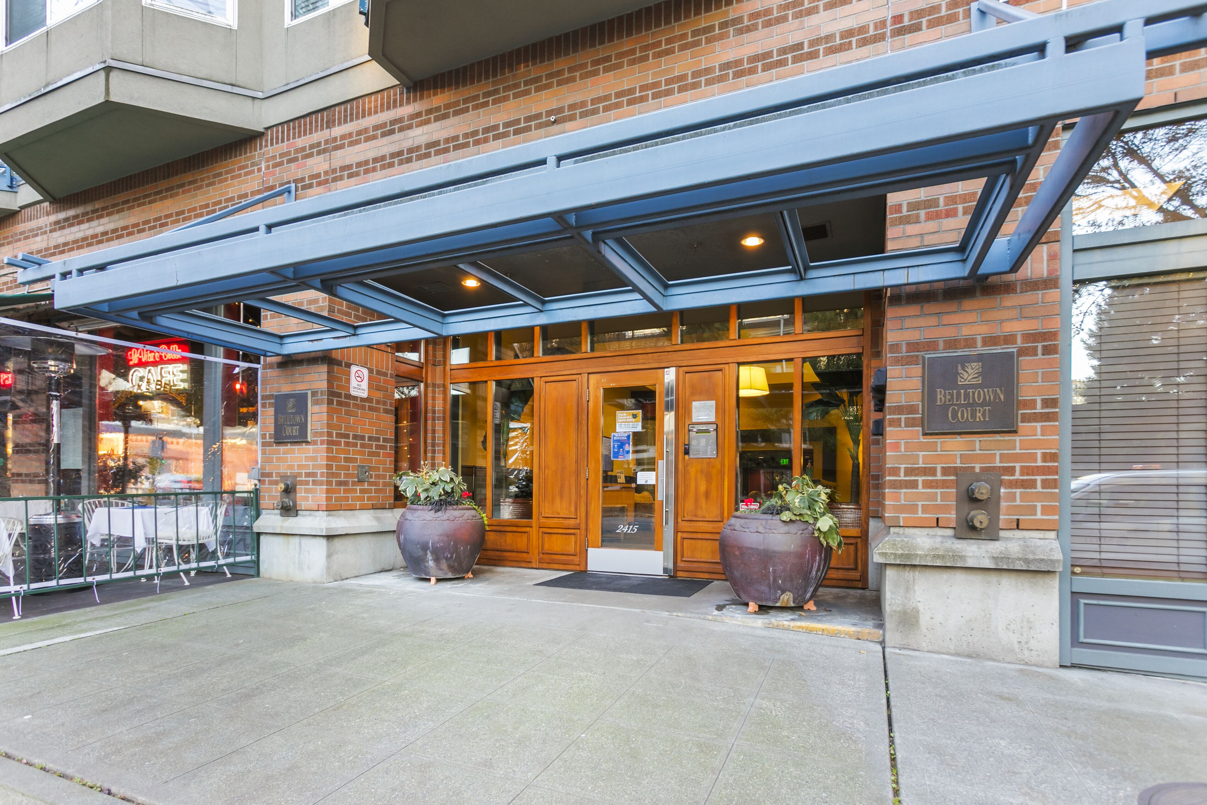 A brick building with a wooden entrance, large potted plants, and a sign that reads "Belltown Court."