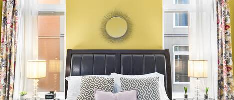 A bed with patterned pillows, a bedside lamp, and a wall-mounted mirror.