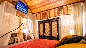 Ein Zimmer mit einem Bett, Vorhängen, einem Fernseher und einem Fenster mit einer Zierverkleidung.