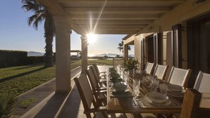 Un área de comedor al aire libre con una mesa dispuesta para seis personas, con vista a un jardín ajardinado y montañas distantes.