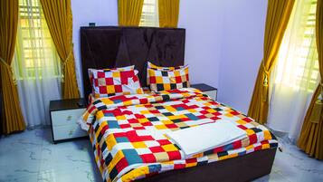 Uma cama bem arrumada com um edredom colorido, uma mesa de cabeceira com abajur e cortinas nas janelas.