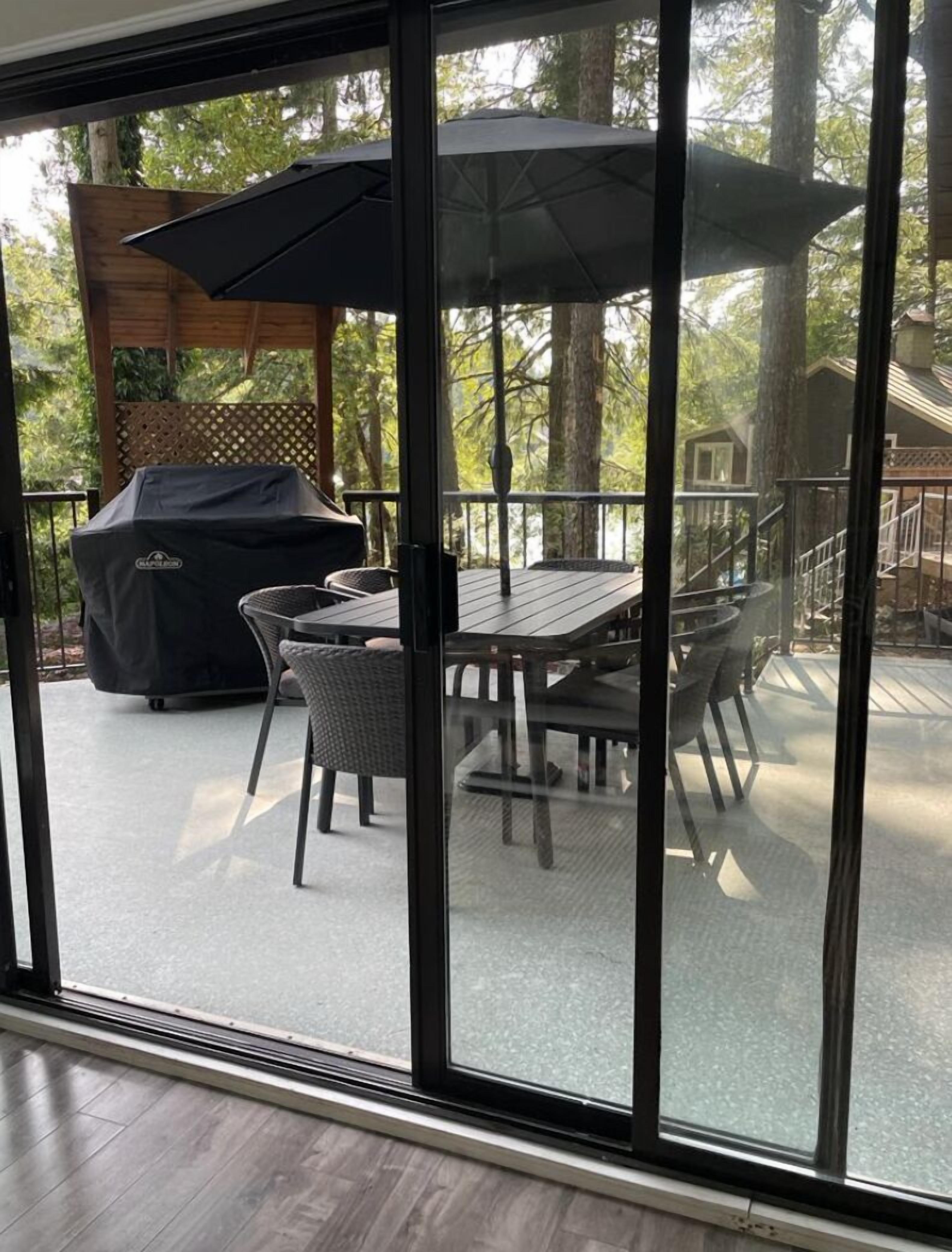 A covered outdoor patio with a table and chairs, a grill, and a wooden deck.