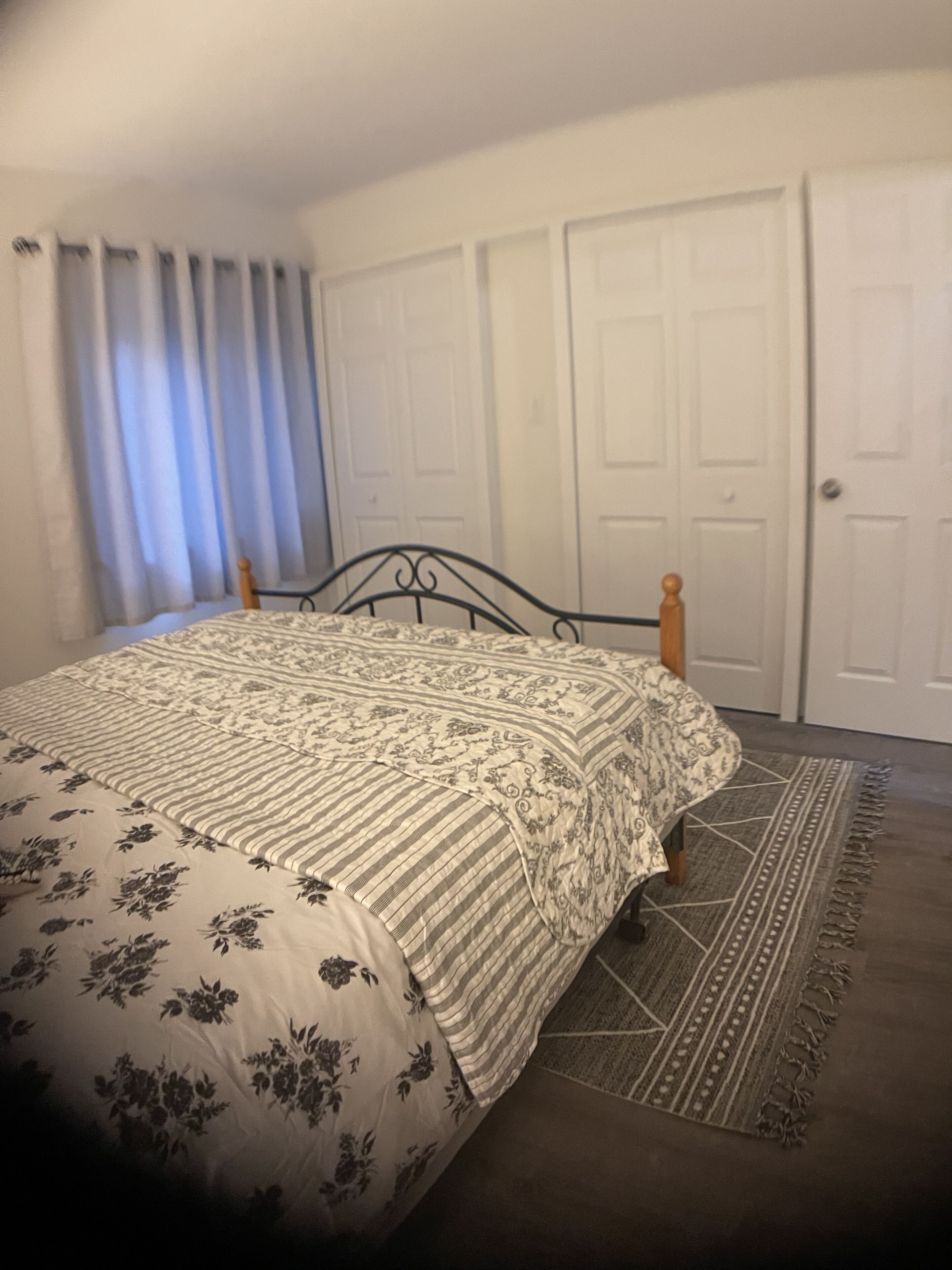 A bedroom with a bed, curtains, a door, and a patterned rug.