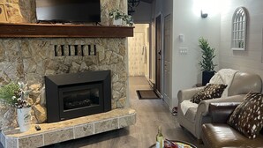 Una sala de estar moderna con chimenea de piedra, sofás de cuero, un televisor de pantalla plana y una mesa de centro con controles remotos.