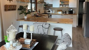 Una cocina moderna con armarios blancos, una isla de madera y una zona de comedor con una mesa negra y sillas estampadas.