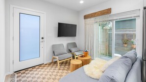 En moderne stue med et fladskærms-tv, to grå sofaer, et sofabord og et stort vindue med gardiner.